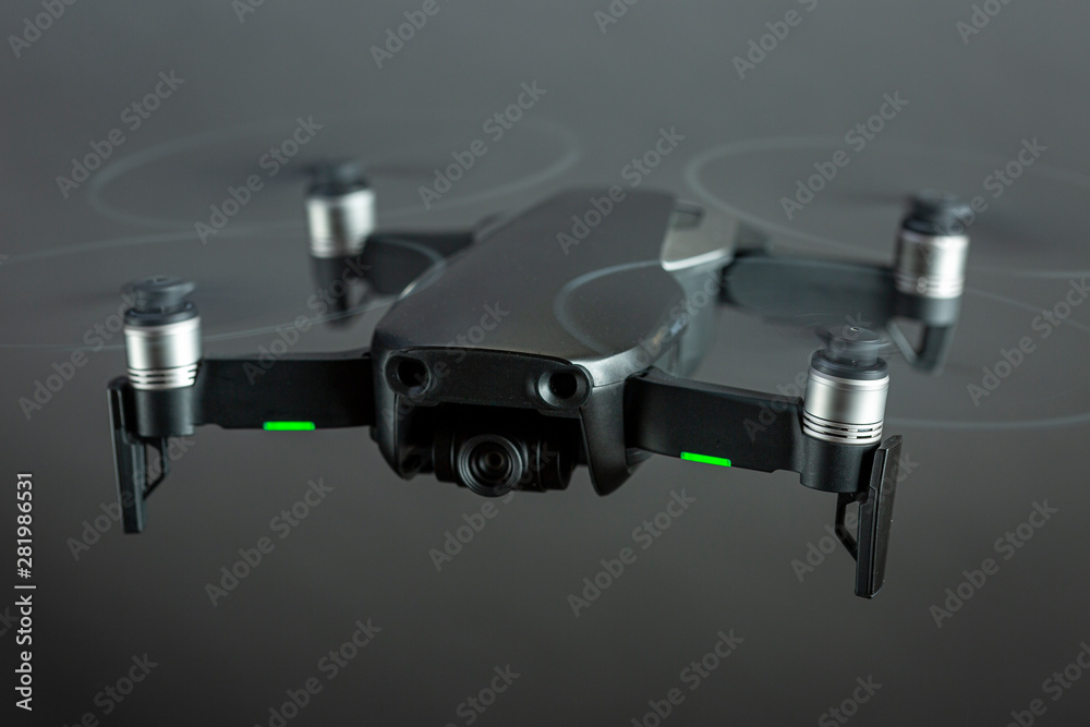 Drone in flight with spinning propellers and green positioning lights on seen from above against a grey even studio background