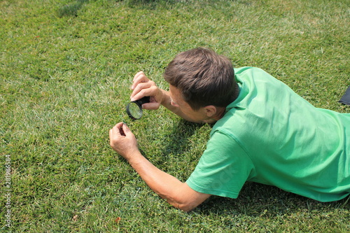 A gardener with a magnifier in his hand checks the grass on the lawn for pests and diseases.