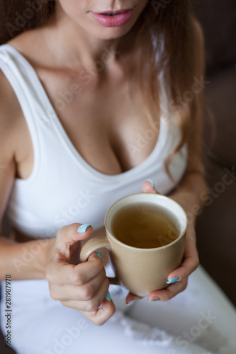 Female hands holding broun cup of tea, color manicure, girl is dressed in white clothes. vertical frame