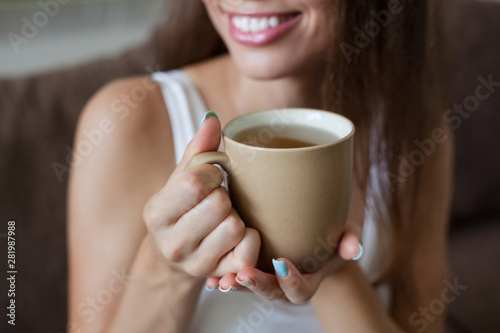 Female hands holding broun cup of tea, color manicure, smiling girl is dressed in white clothes. horizontal frame
