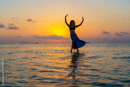 Young beauty girl dancing at tropical beach on sea water at paradise island at sunset. Summer concept. Holiday travel.