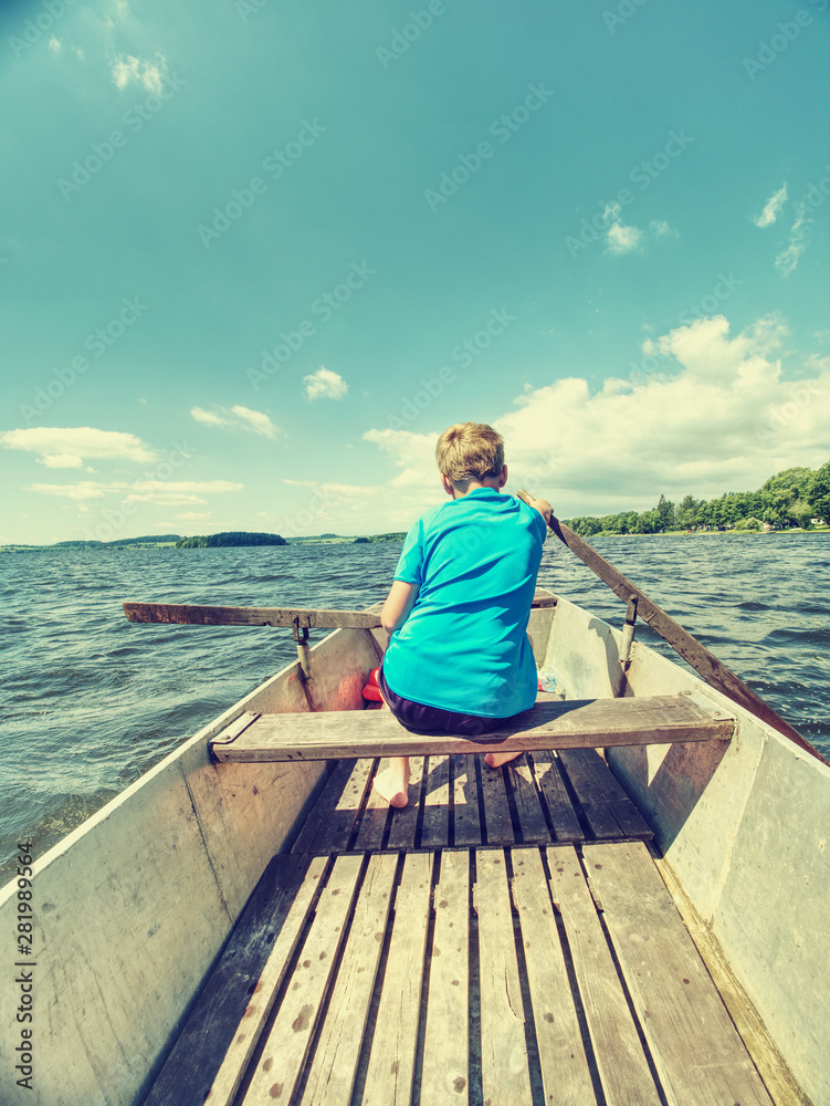 Young teenage boy rowing a rowboat or paddle boat on a lake