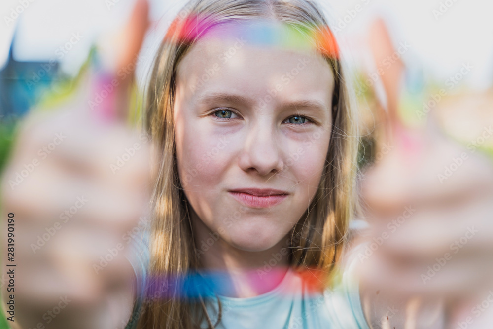 Fototapeta premium the teen girl looks at camera through the colored frame in summer time. 