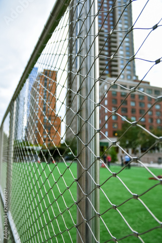 Soccer field concept out of focus in the city of NYC., Manhattan, between skyscrapers. Fence in the foreground focused.