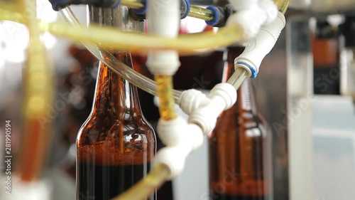 At a brewery, a machine fills a bottle of beer. A machine operator in the background controls the process. Close-up.