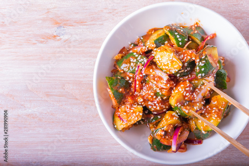Oi Muchim Korean spicy cucumber salad with sesame seeds in a bowl on a wooden table, copy space, top view.