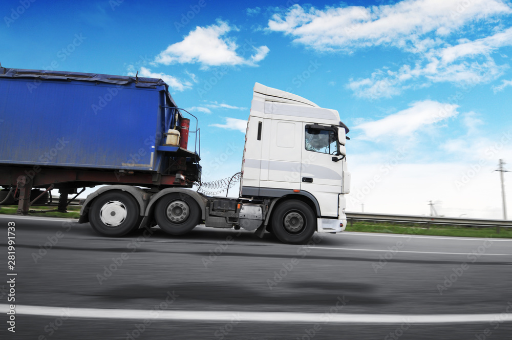 Truck with a trailer in motion on the countryside road against sky with clouds