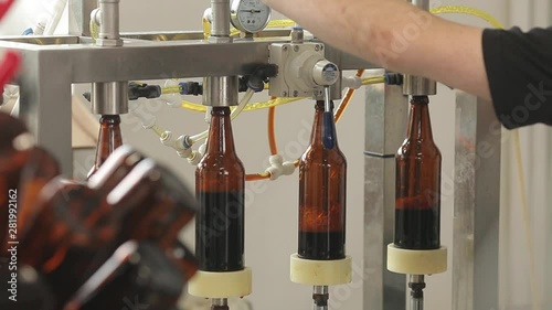 At a brewery, a machine fills a bottles of beer. A machine operator controls the process. Close-up.