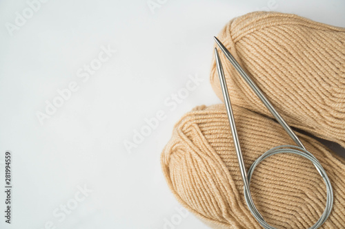 Knitting needles and two skeins of beige wool yarn on a white background. Copyspace. For for yarn stores, needlework, banner design.