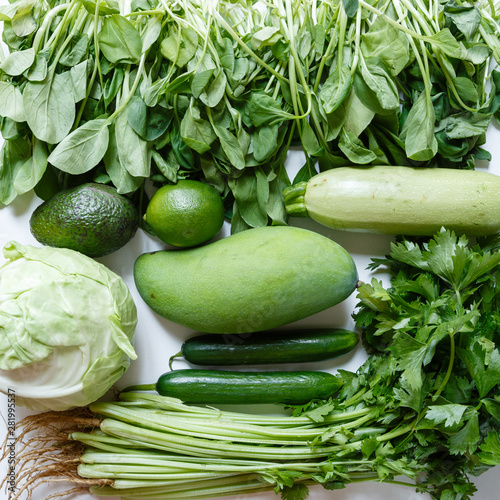 Fresh green vegetables variety on rustic white background from overhead, celery, avocado, cabbage, mango, cucumber, spinach, lime, squash. Healthy, vegetarian concept. Flat lay, top view