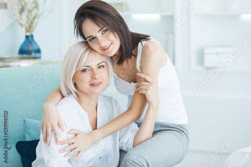 Mature mother and her adult daughter together. Women indoors portrait. Middle age woman and her daughter at home sitting on the couch.