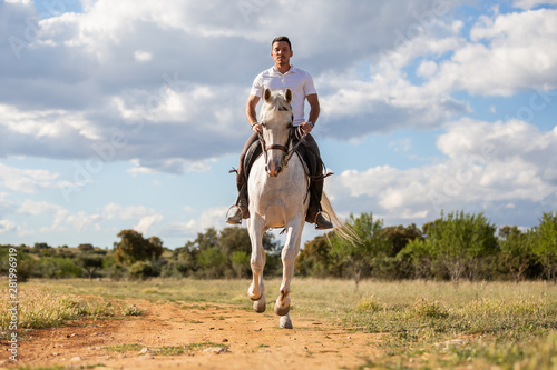 Young guy in casual outfit riding white horse on sandy road © pablobenii