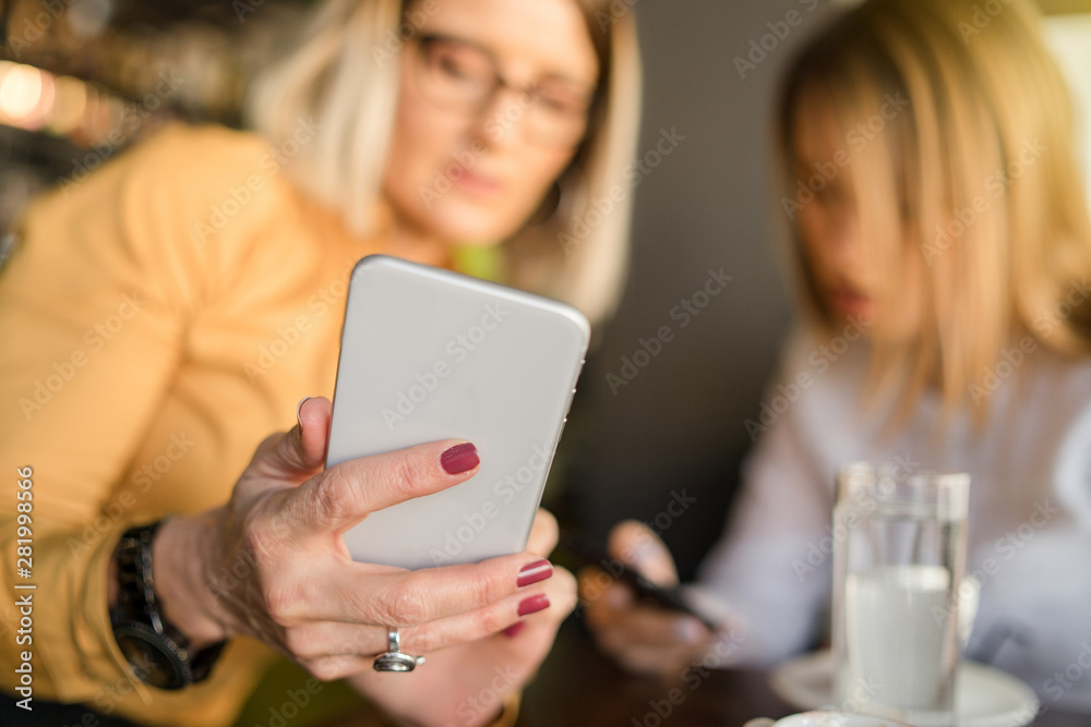 Two Business women using smart mobile phones app on a coffee brake at the company Two Business women using smart mobile phones app on a coffee brake at the company