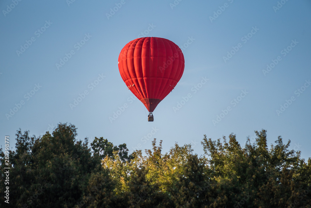 Red hot air balloon in the sky above the trees