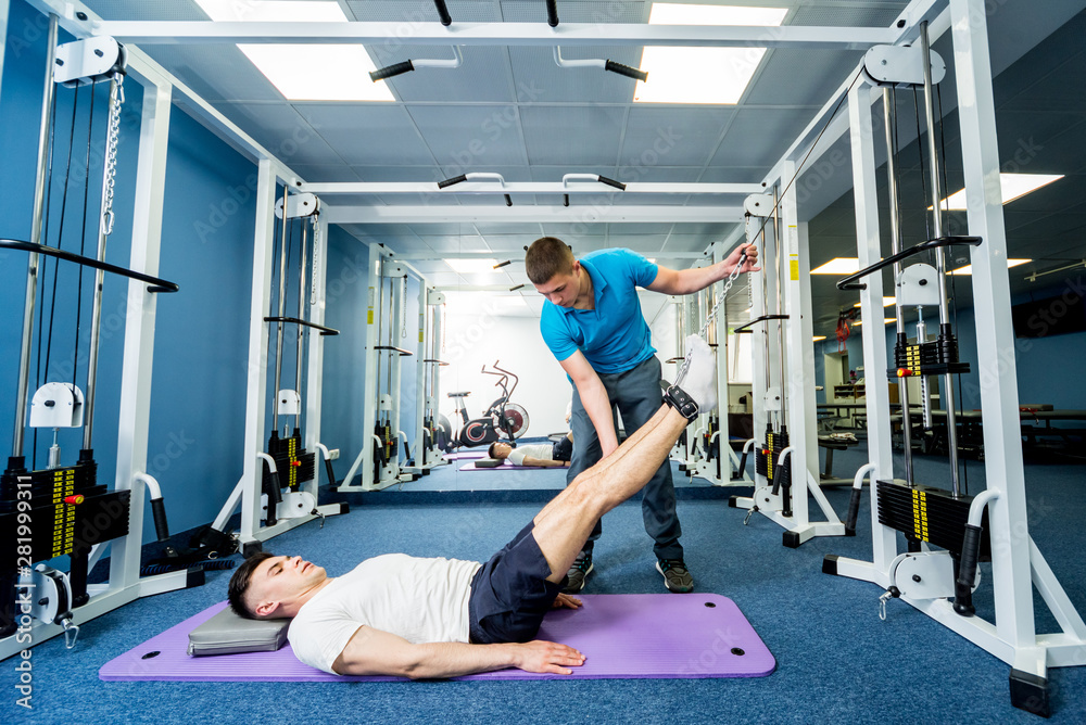 Rehabilitation therapy. Young man doing exercises on mat under supervision of physiotherapist. Rehabilitation therapy. Young man doing exercises on mat under supervision of physiotherapist.