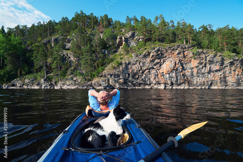 The hostess and the dog are sailing in a kayak boat near the rocky shore.
