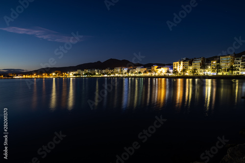 Long exposure of a coastline at night over the sea with city lights © Gabriel