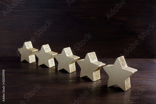 five golden stars on dark wooden background, top rating concept