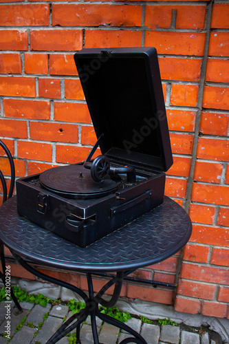 Old black mockup vintage gramophone on the metal table on the background of red brick wall. Outdoors. Vertical. Urbal design, Creative. photo