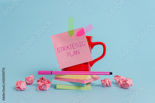 Writing note showing Strategic Plan. Business concept for A process of defining strategy and making decisions Coffee cup pen note banners stacked pads paper balls pastel background