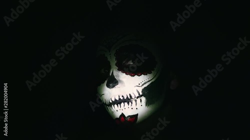 Halloween mask. A girl in a blinking and frightening light. Mexican day of the dead. Portrait of a young woman with scary makeup for Halloween on a dark background. 4K