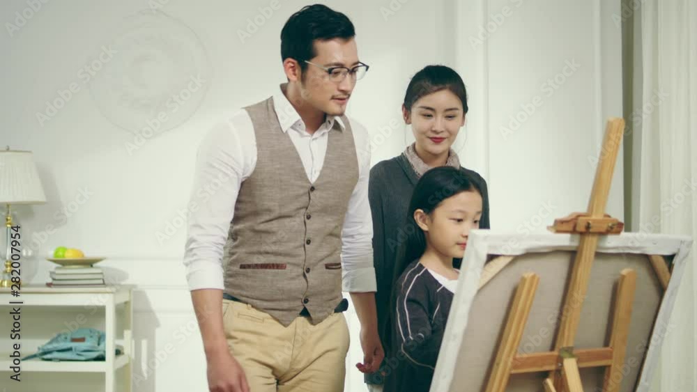 nine-year-old little girl making a painting with two parents standing behind watching encouraging and providing guidance nine-year-old little girl making a painting with two parents standing behind watching encouraging and providing guidance