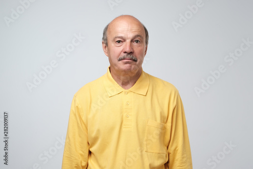 Sad upset mature hispanic guy in yellow pullover looking with guilt and sadness. Studio shot