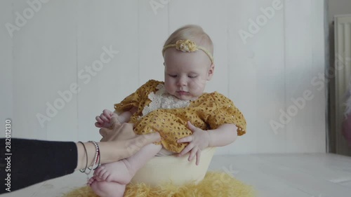 A little girl in a yellow dress and flowered yellow hair band is sitting in an egg shell as a chick photo