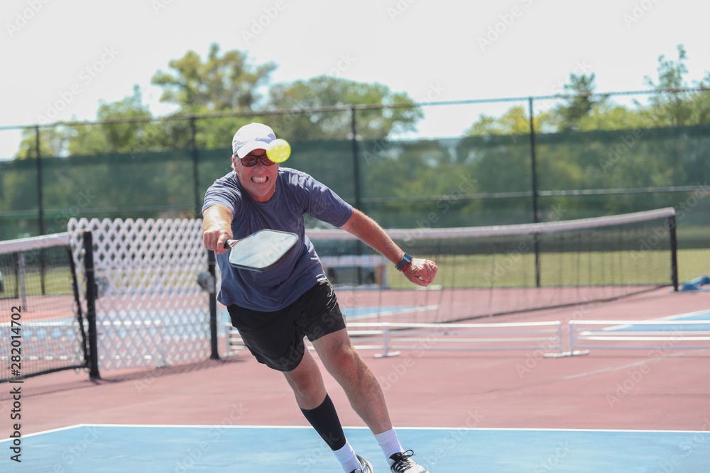 A senior man hits a shot while competing in a pickleball tournament