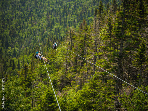 man and woman zipline down mountain above forest