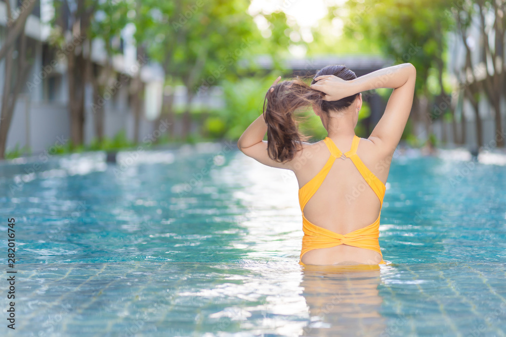 Rear view of a Asian beautiful woman in a sexy yellow swimsuit. She standing in the swimming pool and tied her hair in ponytail.
