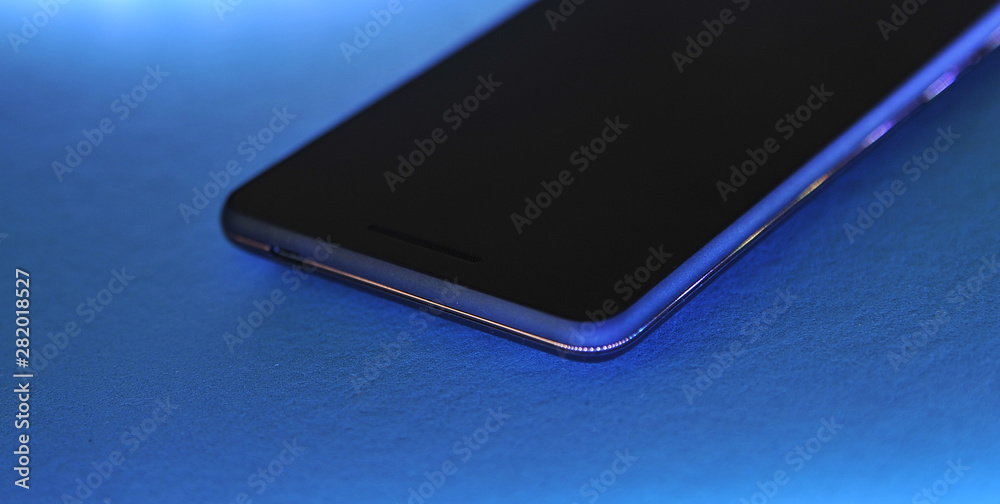 Black touch phone on blue background in neon light. Black touch phone on blue background in neon light.