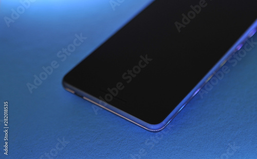 Black touch phone on blue background in neon light.