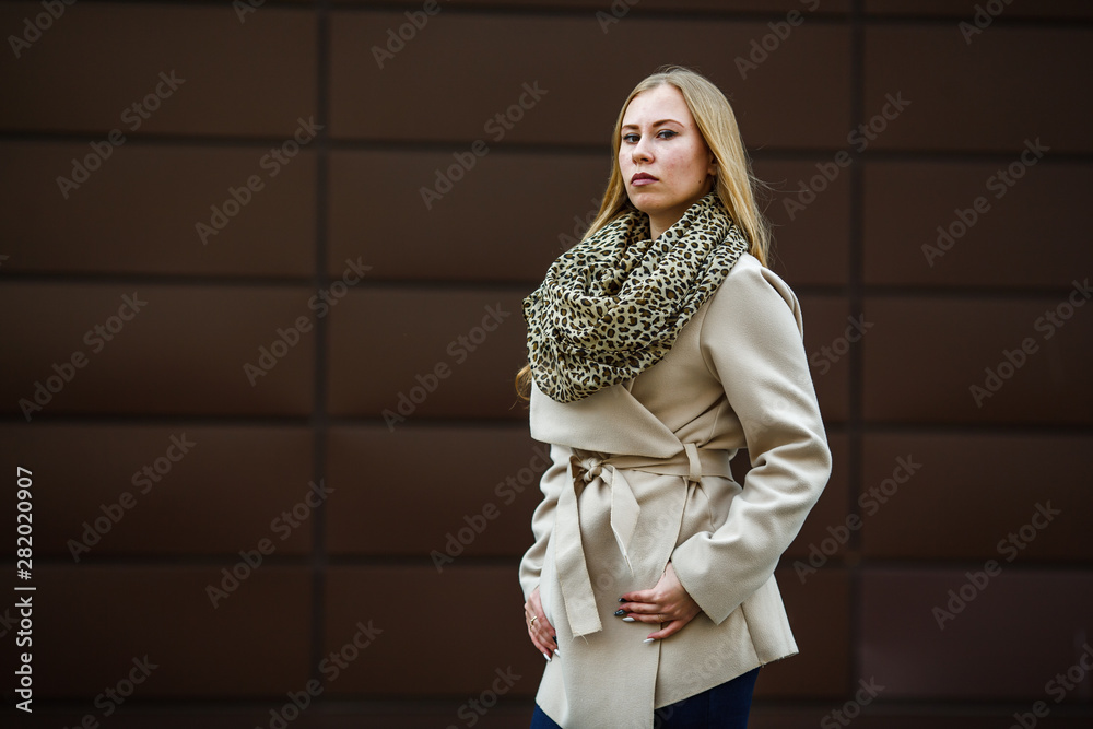 Portrait of a young cute caucasian girl with problem skin in scarf and cream coat opposite brown background on the street in spring. Portrait of a young cute caucasian girl with problem skin in scarf and cream coat opposite brown background on the street in spring.