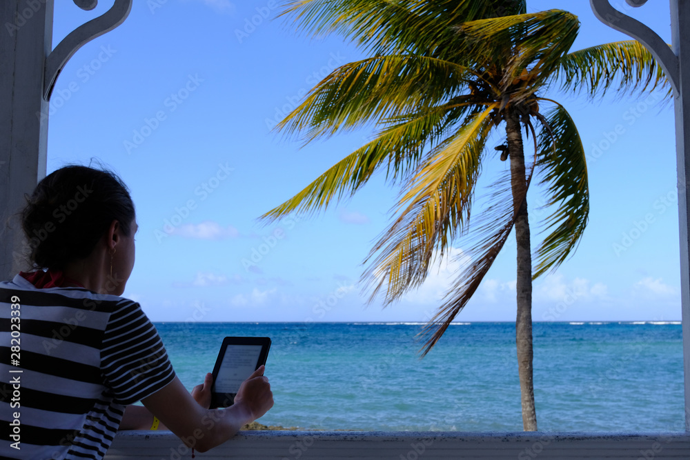 A lady reading electronic book on a beach in a sunny day