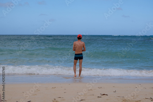 Man standing on the beach of the sea in swimsuit and red hat. 