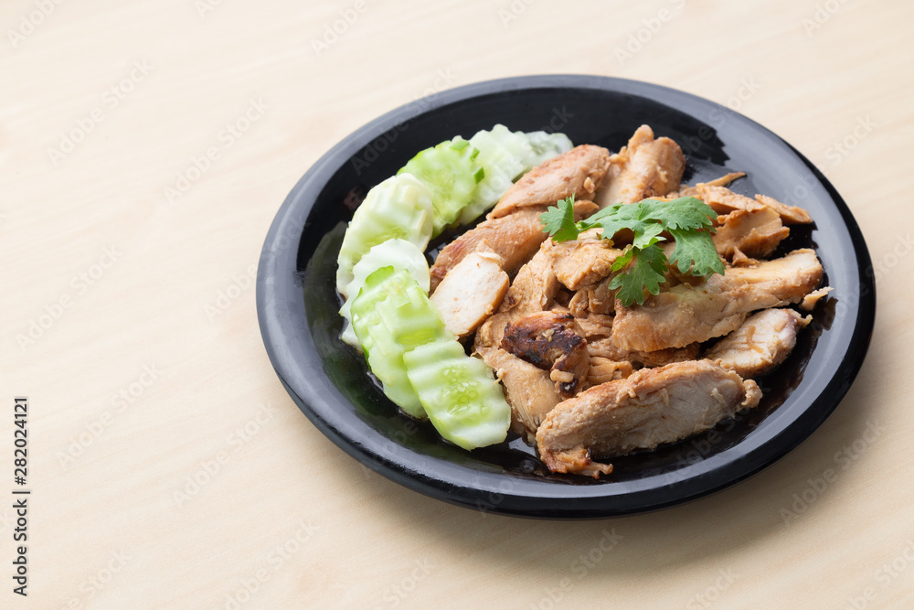 Partially sliced grilled chicken breast with cucumber in black plate on wooden table.