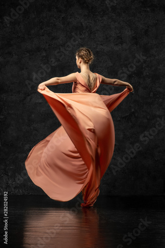 Ballerina. A young dancer dressed in a long peach dress, pointe shoes with ribbons. Performs a graceful, graceful dance movement  which is visible from the back. Beautiful classic ballet. 
