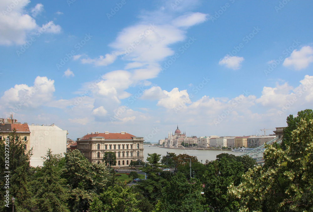 View on a city with buildings, river, green trees and cloudy sky