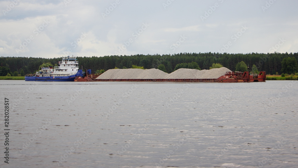 Pusher tug boat carries a loaded barge cargo ship with gravel on the river, logistics of cargo transportation by water transport
