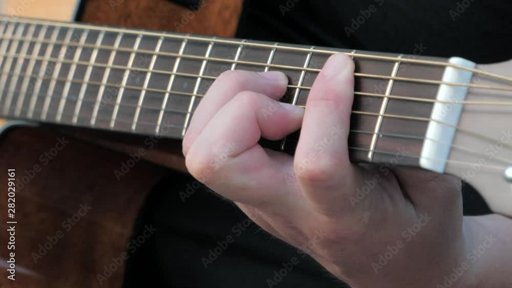 Close-up side angle shot of fingers playing a guitar. Musician clamps the chords on the guitar frets. Close-up side angle shot of fingers playing a guitar. Musician clamps the chords on the guitar frets.