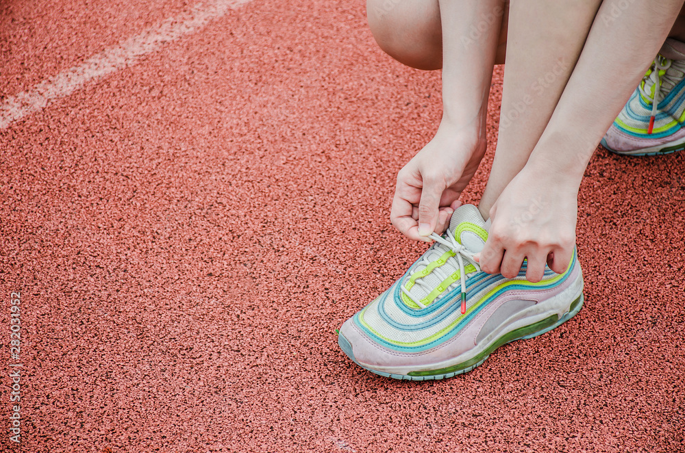 Running shoes - closeup of woman tying shoe laces. Female sport fitness runner getting ready for jogging outdoors on the lanes of a track