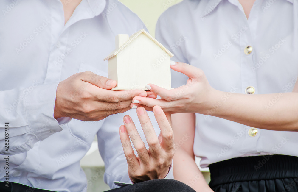 Closeup hands of an couple students holding a little house together, Concept of sustaining a house between two people. Helping your partner in owning a house.