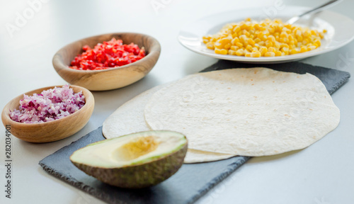 Ingredients for Mexican vegetarian tacos in bowls on light table, close-up