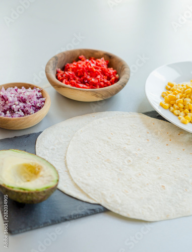 Ingredients for Mexican vegetarian tacos in bowls on light table  close-up
