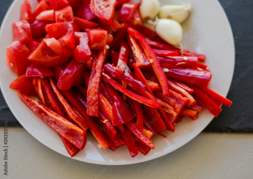 Slices of fresh red hot chili peppers and tomatoes with garlic on white plate, close-up Slices of fresh red hot chili peppers and tomatoes with garlic on white plate, close-up
