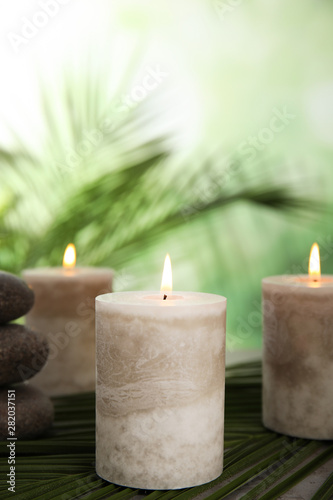 Burning candles and spa stones with palm leaf on table against blurred green background, space for text