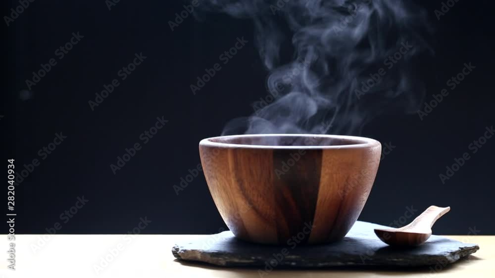Selective focus of smoke rising with hot soup in cup on dark background