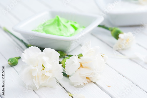 night cream with white carnation flowers on bright wooden table background