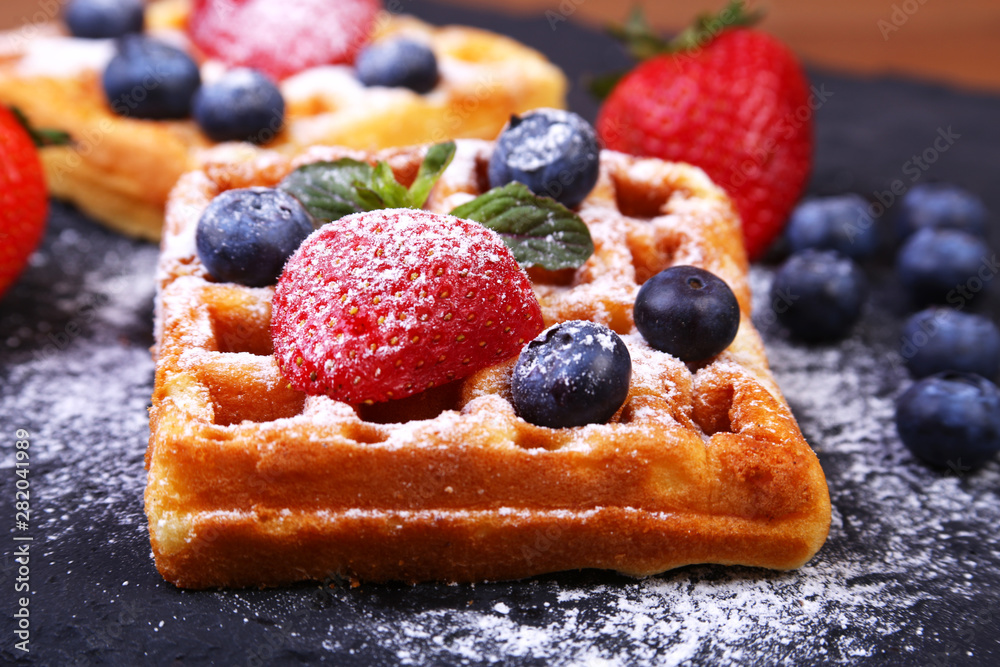 Homemade Traditional belgian waffles with fresh fruit, berries and sugar powder on black plate.